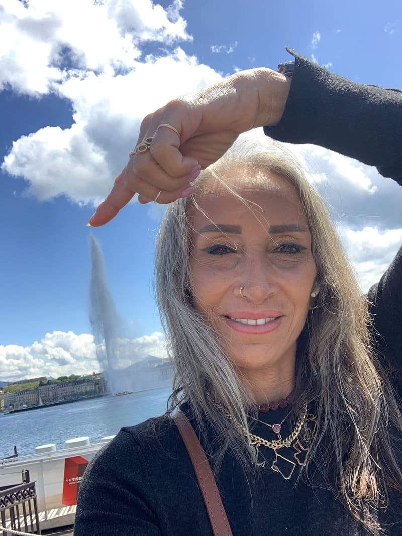 Lina smiling by Lake Geneva, hand raised to frame the light