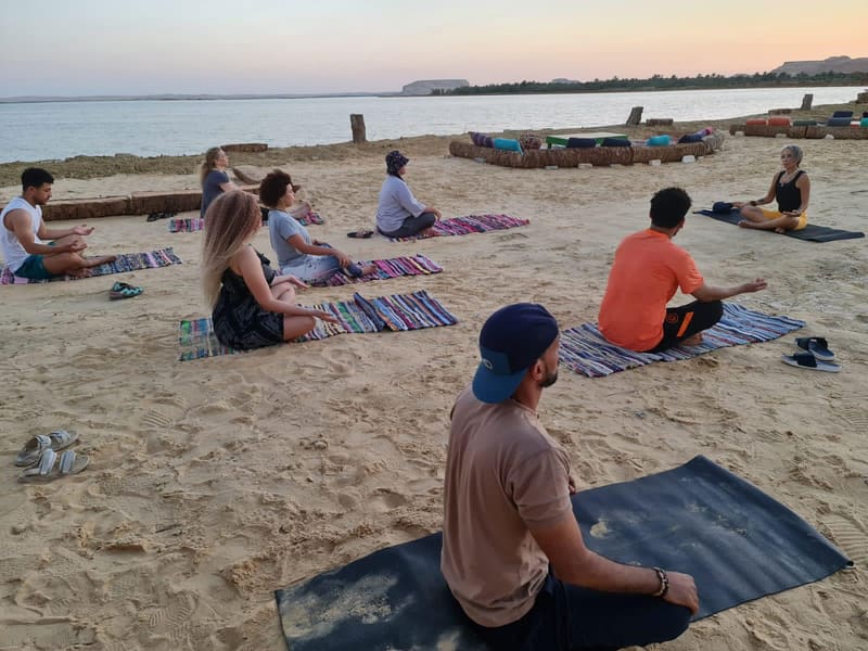 A group meditating on woven mats on the sand by the salt lake, Siwa